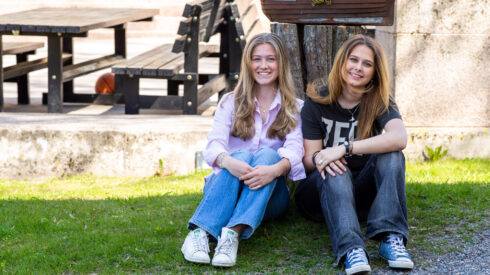 _R9Q7676 Två kvinnliga elever sitter på gräsmatta framför skolan